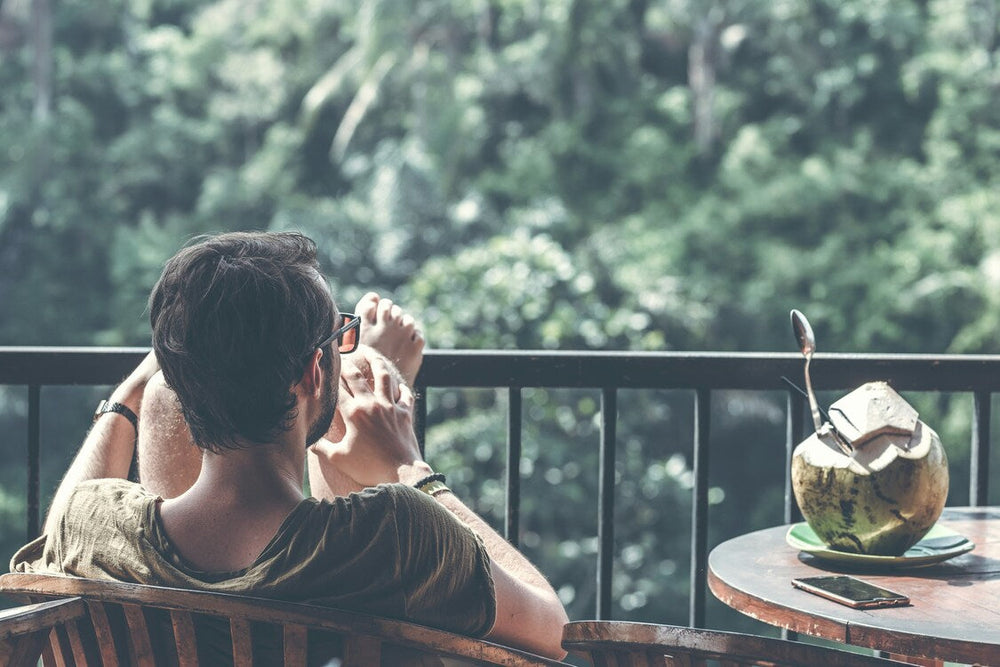Bărbat relaxându-se pe terasă, privind natura tropicală, asociat cu beneficiile centurii cu turmalină pentru relaxare și energie